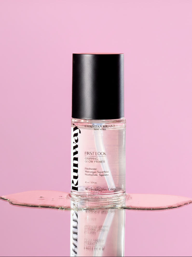 Christian Siriano Runway First Look Gripping Glow Primer in a clear bottle with black cap, displayed on reflective surface against a pink background.